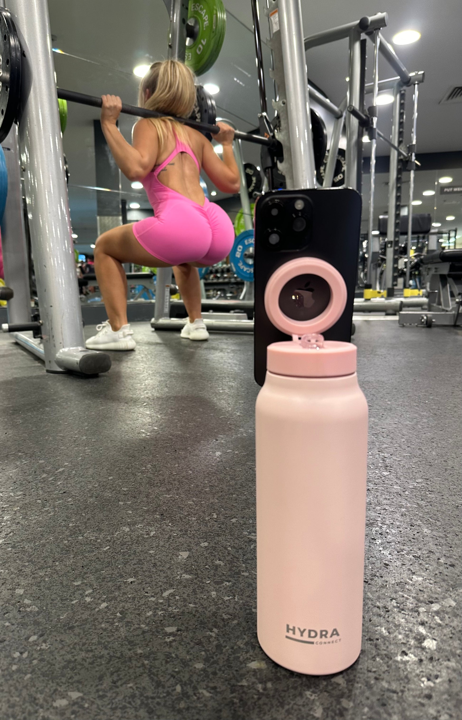 Pink water bottle with pink lid on a gym floor, person exercising in the background