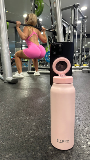 Pink water bottle with pink lid on a gym floor, person exercising in the background